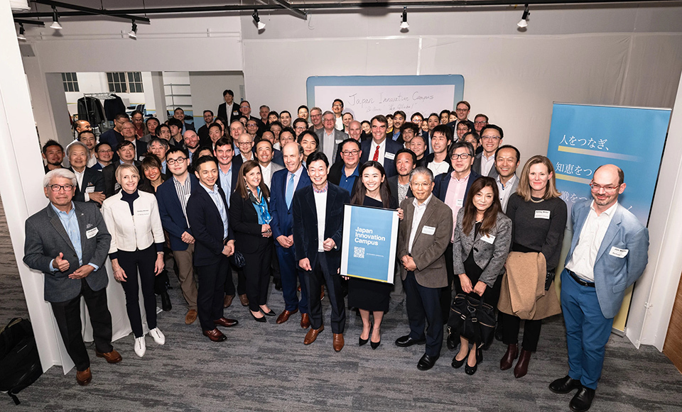A group of professionals in business attire gathered for a photo in an indoor setting, holding a framed JIC poster.