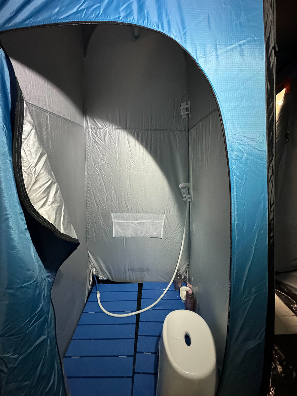 Interior of a portable, blue shower tent with a reflective lining, blue ground boards, and a white shower head.