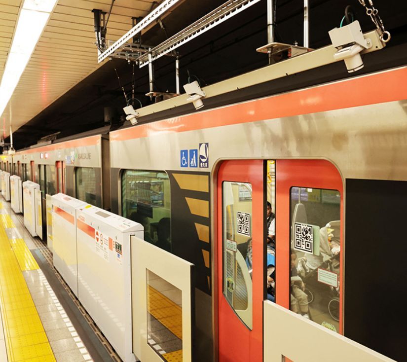 A Toei Subway Station in Tokyo. Red and silver train cars with red doors sit at the platform, ready for boarding.