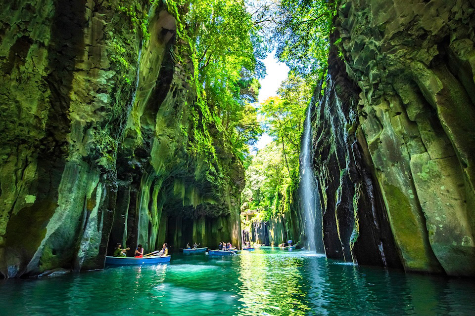 Gorge with boats on a turquoise river and a waterfall.