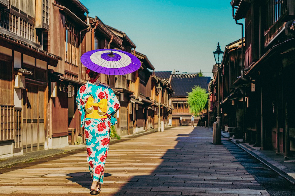 Person in traditional Japanese attire with a purple umbrella walking down a street.