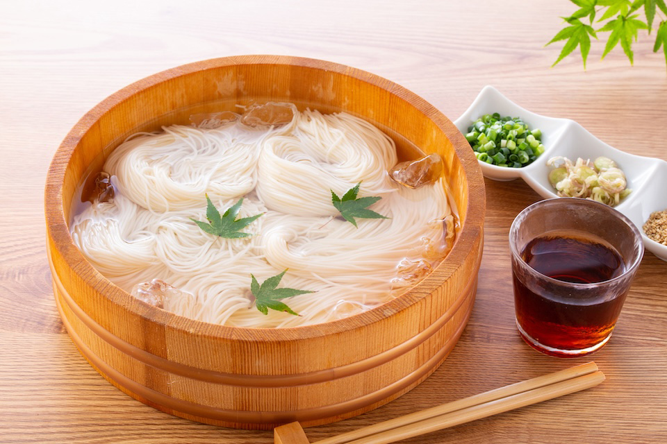 Wooden bowl of somen noodles with garnishes and a  somen soup.