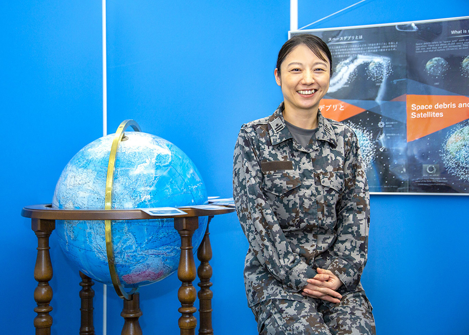 Lieutenant Colonel KANAGAWA Ayumi of the Japan Air Self-Defense Force, in military attire seated next to a globe on a table.