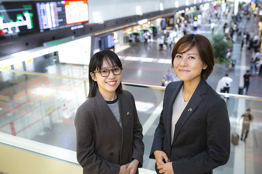 Two women in business attire at airport terminal.