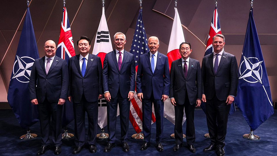 Group photo of six world leaders standing in front of flags, including Japan, Australia, New Zealand, the Republic of Korea, and the United States, with NATO flags on either end.