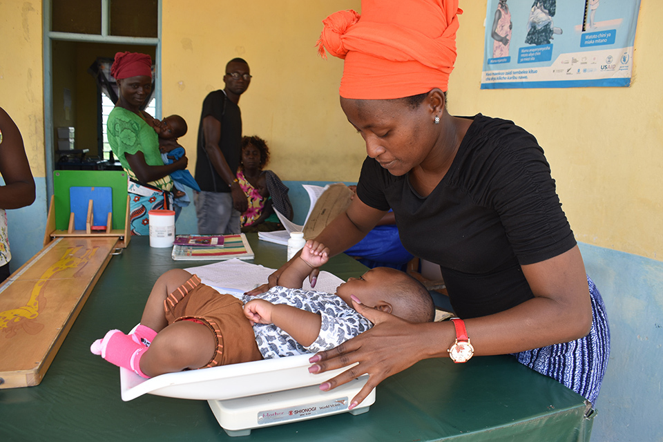 A  health service volunteer weighing a baby on a scale in a clinical locating in Kenya.