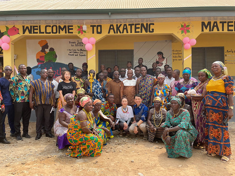 A group of people gathered in front of a maternity waiting house with the sign ‘WELCOME TO AKATENG’ above the entrance.