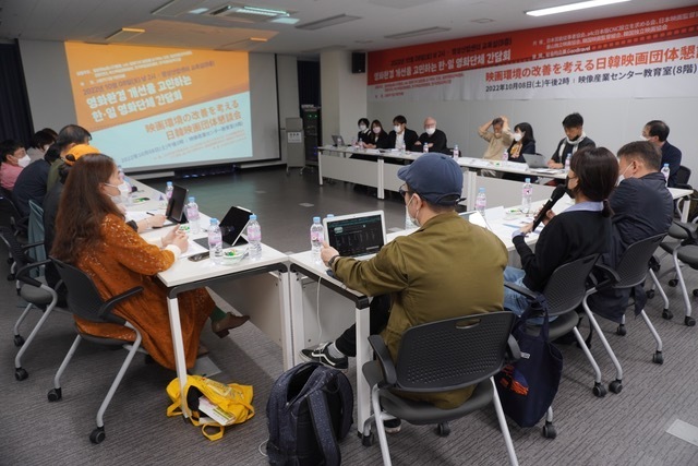 A group of people sitting around a large conference table, participating in a meeting.