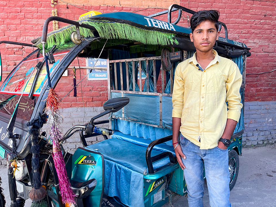 A young taxi driver in India stands beside Terra Motors' electric three-wheel auto-rickshaw with coloful decoration, purchased with the company loan.