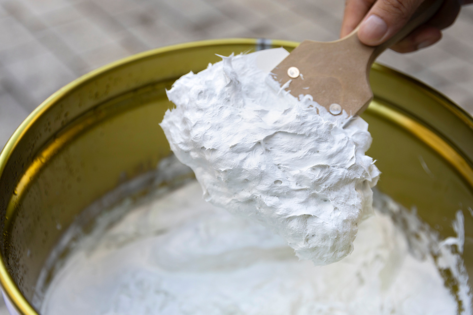 A close-up view of a spatula covered with a white Aster Power Coating is being held over a large round container.