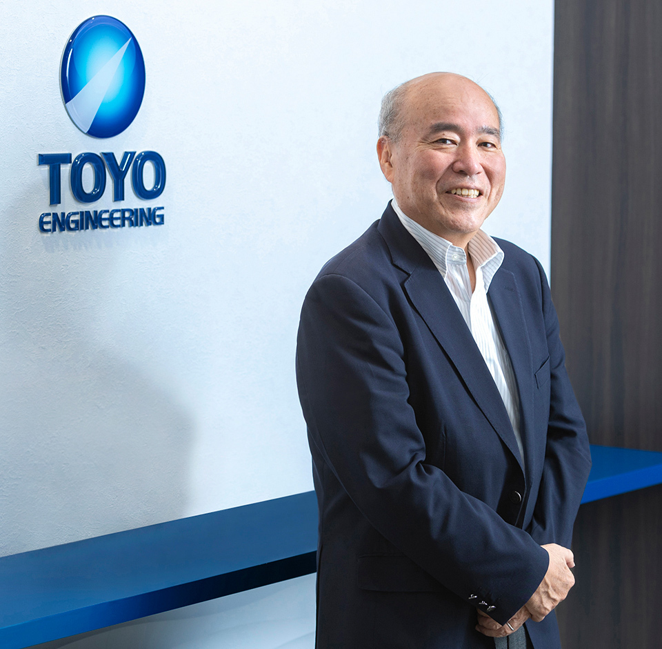 Executive officer of Toyo Engineering, wearing a dark suit and white shirt, standing beside the TOYO Engineering logo.