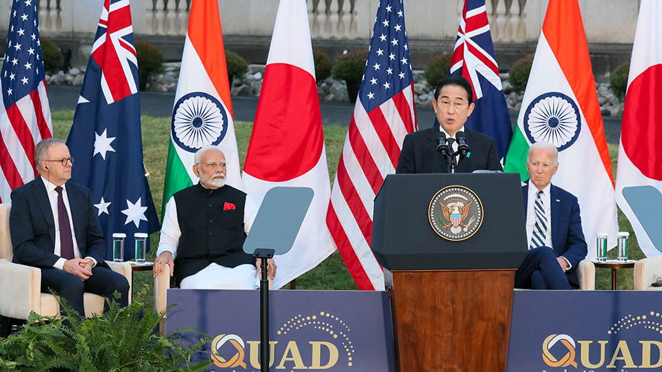 The leaders stand together in front of four respective national flags - the American flag, Australian flag, Indian flag, and Japanese flag.