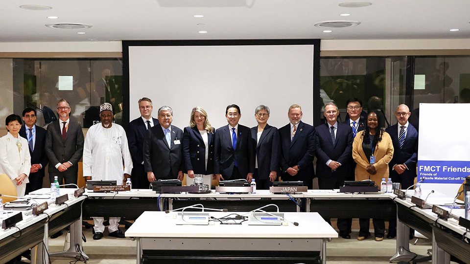 A group photo of delegates standing behind conference tables in a meeting room.