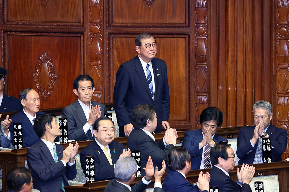 A group of congressmen in formal attire clapping to the new PM at the Chamber of the House of Councillors.