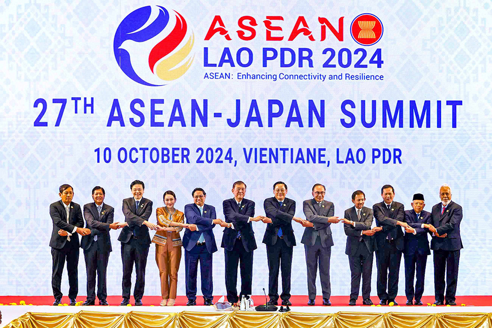 The leaders of the ASEAN member states and Japan, with Timor-Leste as an observer, stand in a line, crossing arms with those beside them.