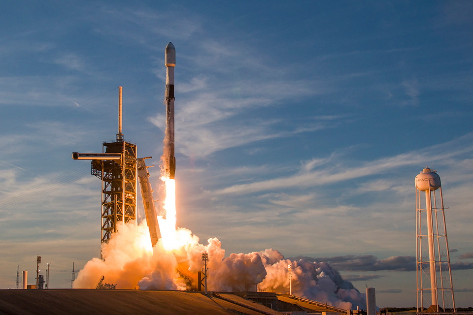 A rocket launches into a clear sky from a launchpad, leaving a trail of smoke and flames as it ascends.