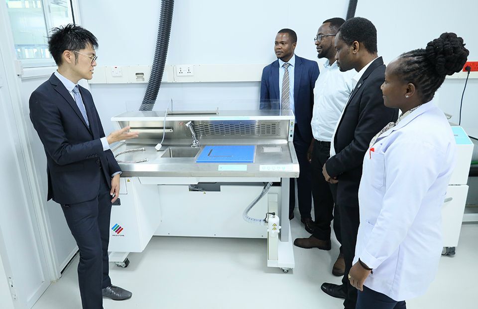 A group of professionals in suits discussing a pathology test while gathered around a machine in the testing facility.