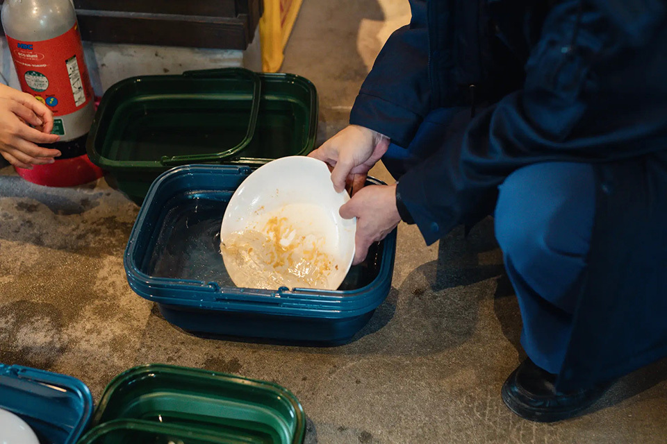 A man put a dirty plate into a bowl on a ground, showing how to use water-saving dishware.