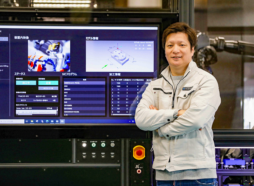 HIRAYAMA Takayuki, CEO of ARUM Inc., the developer of ARUMCODE, standing in front of a large screen displaying various data for component machining.