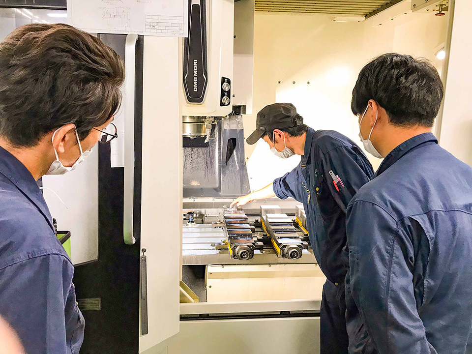 Three technicians in blue shirts conduct machining tests at a component machining subsidiary of ARUM Inc.