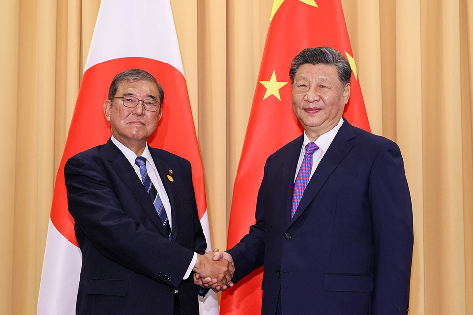 Two men shaking hands and the Japanese and Chinese flags in the background.