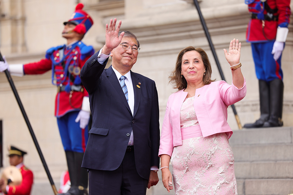 A man and woman in formal attire wave to an enthusiastic crowd, showcasing a moment of celebration.