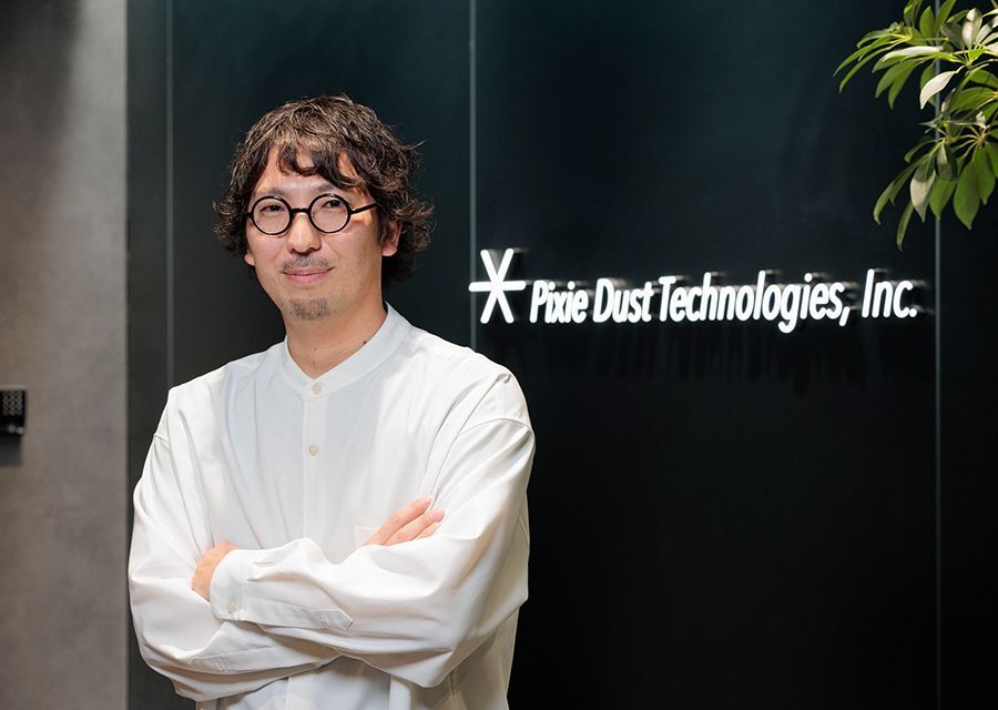 A man wearing glasses stands before a wall displaying the words "Pixie Dust Technologies, Inc." in a professional setting.