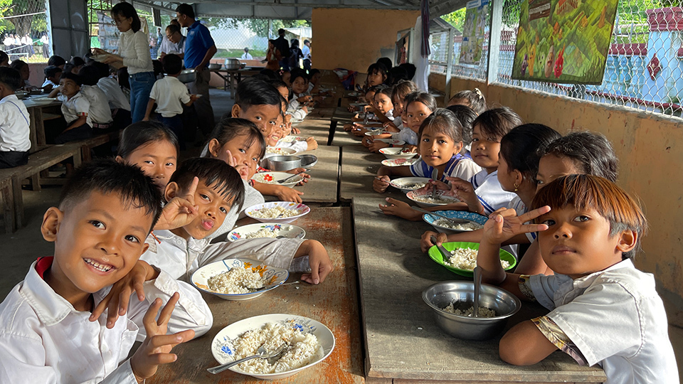 Children enjoying lunch together at a school cafeteria, sharing smiles and food in a lively atmosphere.