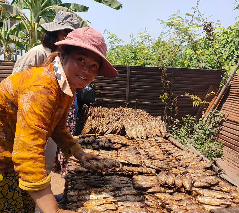 A woman stands next to a table with an array of fish and introduces the smoked seafood.