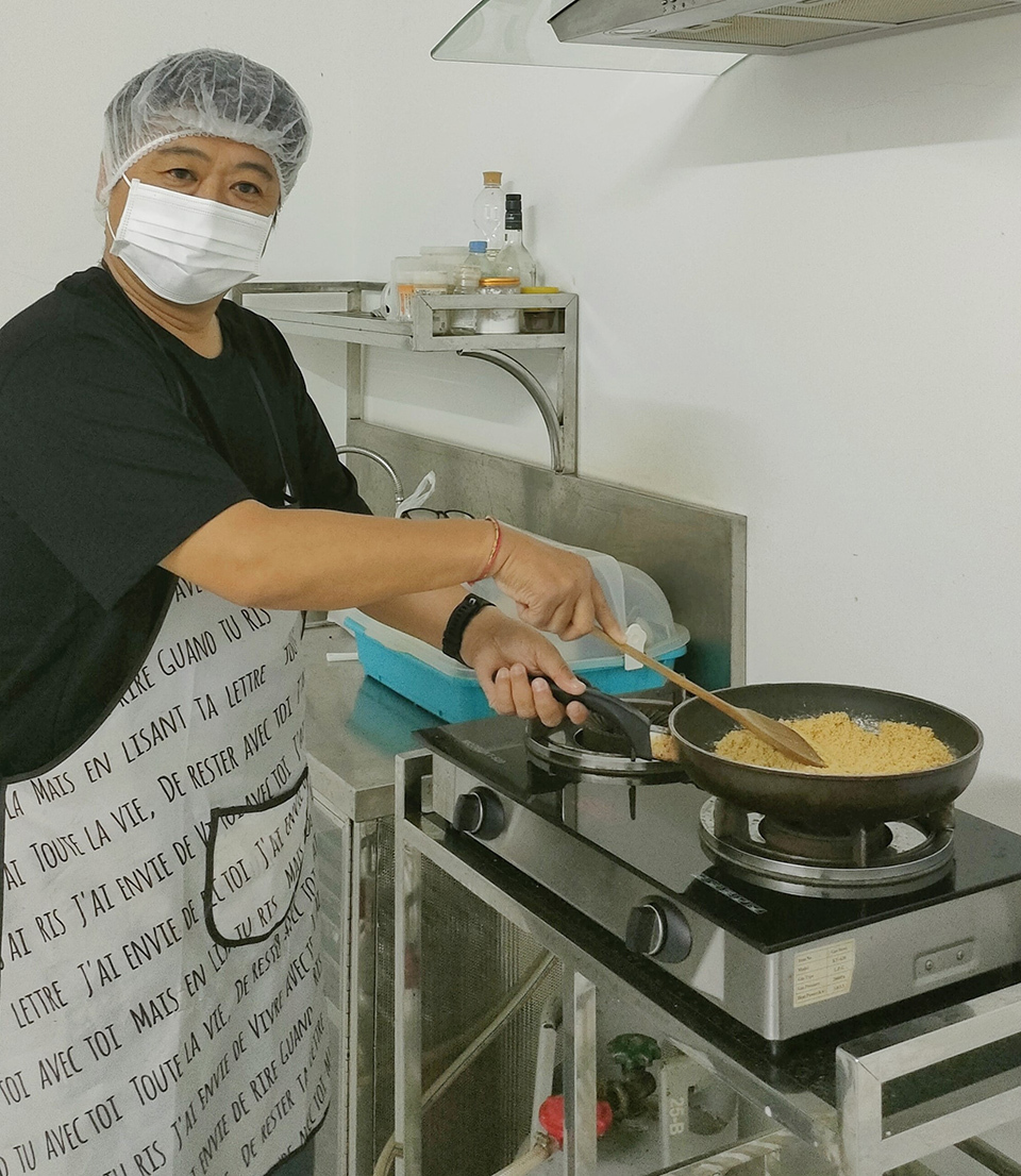 A man in a mask and gloves prepares food in a kitchen, ensuring safety and hygiene while cooking.