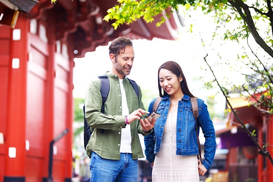 Young male and female tourists looking at their cell phone in front of the red gate.