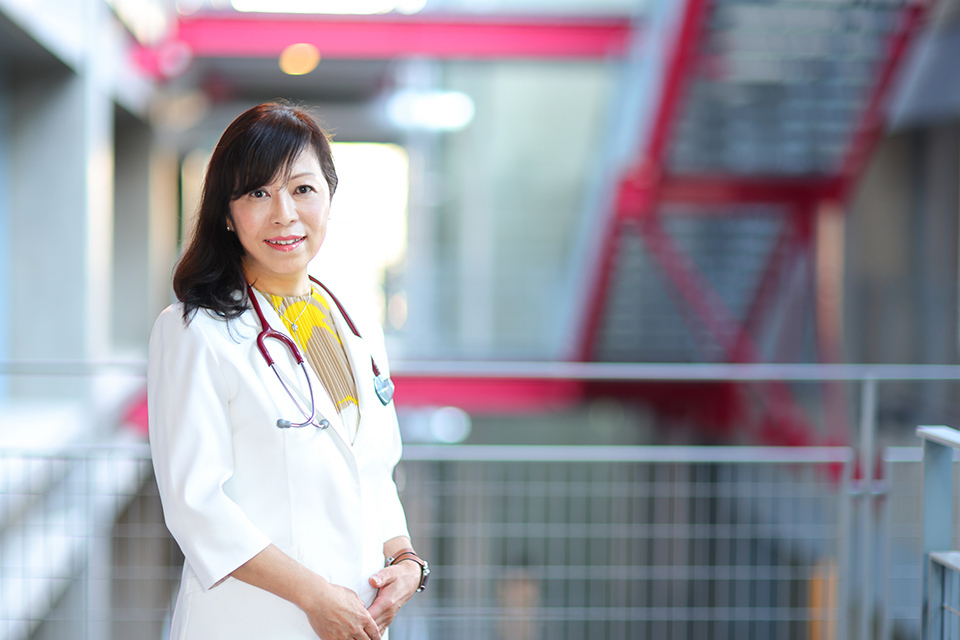 A woman in a white coat poses in front of a stairwell, embodying a sense of determination and professionalism.