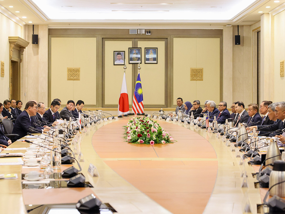 A large meeting room filled with attendees seated at a oval long table during the Japan-Malaysia Summit Meeting.