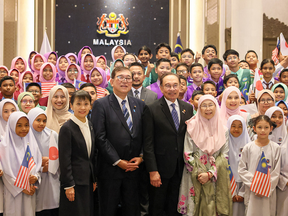 A group photo of Malaysian students wearing hijabs and government representatives posing together in a formal setting.