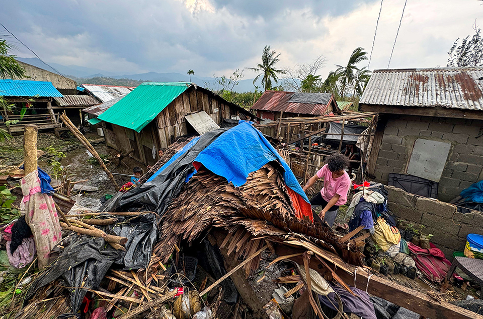 A individual wearing pink shirt stands on a large pile of debris, searching for something, in the Philippines. The area was hit by Typhoon Yingxing in November 2024.