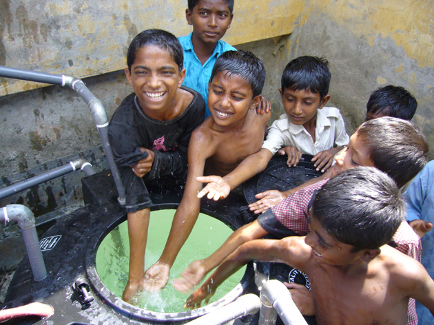 Children happily gather around a water well, enjoying the refreshing water on a sunny day.